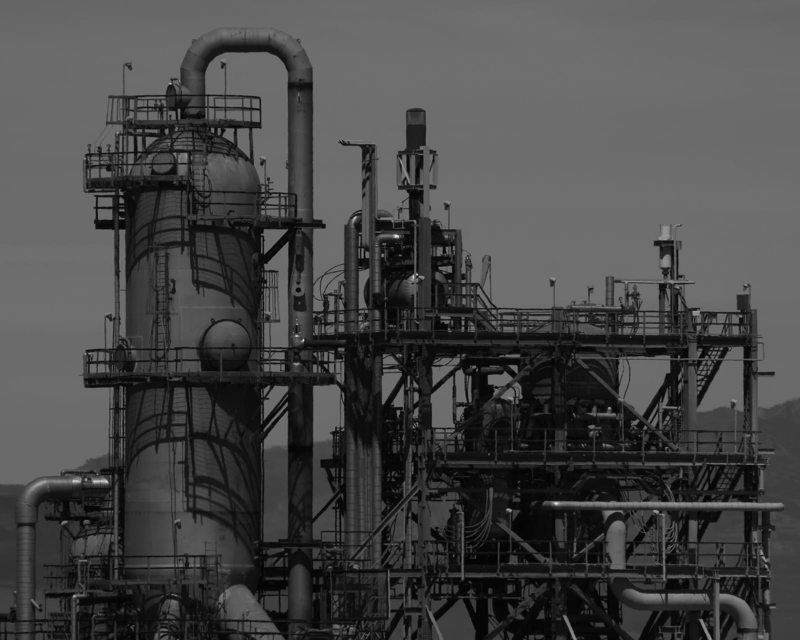 Process towers, pipework and steel walkways of an industrial plant against a hazy sky